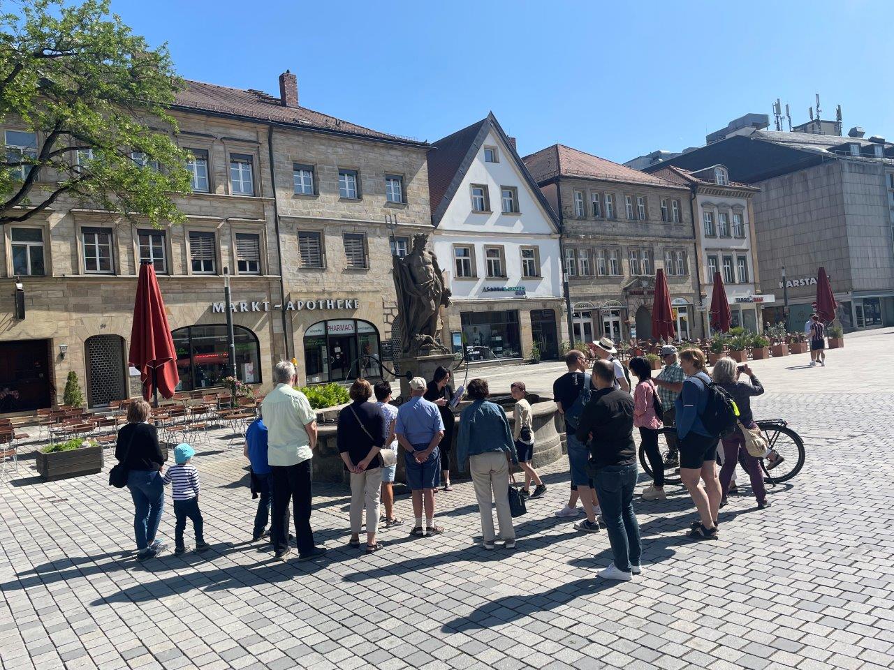 Stadtführung vorm Brunnen auf dem Markplatz vor Häusern.